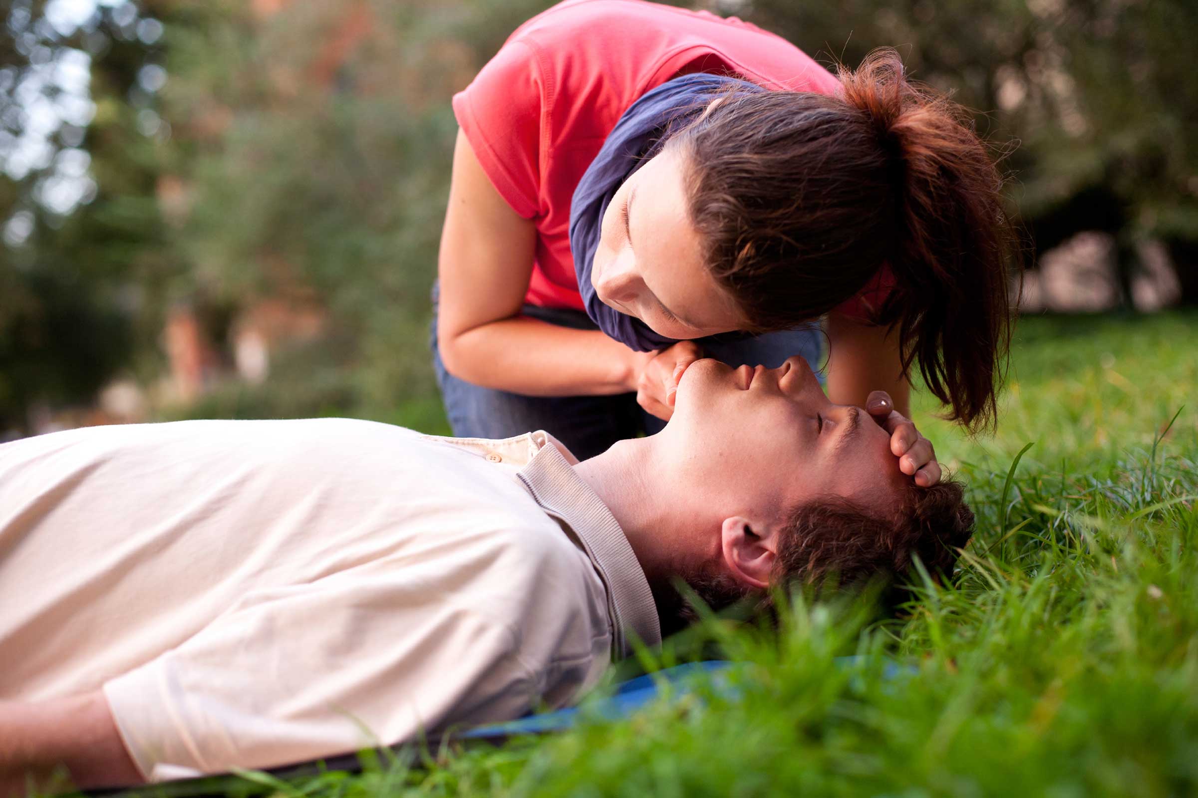 A person performing a breathing check on an unconscious male, illustrating the importance of CPR training in responding to cardiac emergencies.