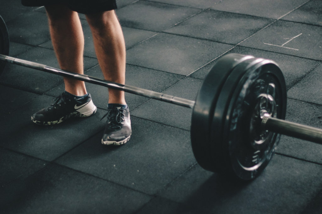 Close-up of a barbell with a lifter preparing to deadlift, promoting exercise as a way to lower heart disease risk.