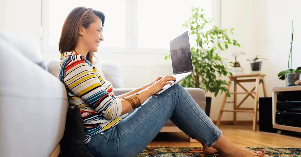 A woman sitting on the floor at home using a laptop to complete an online CPR and First Aid certification course.