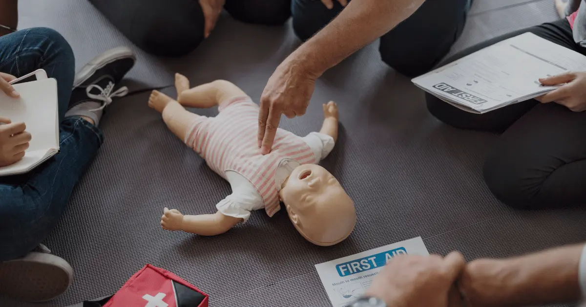Instructor pointing out correct chest compression spot on infant CPR manikin during First Aid class